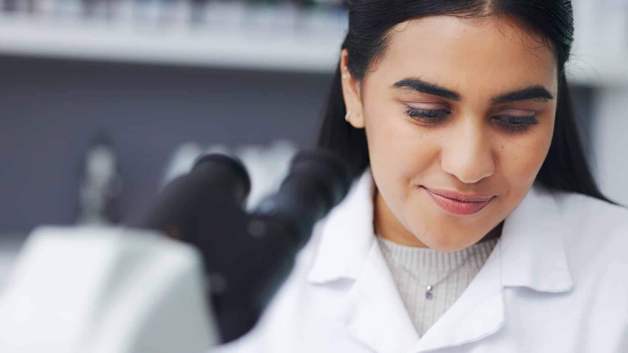 Young scientist using a digital tablet and microscope in a lab. Female pathologist analyzing medica